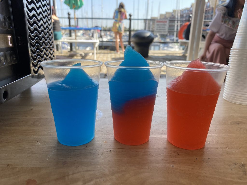 Blue and red slushies in cups by a marina